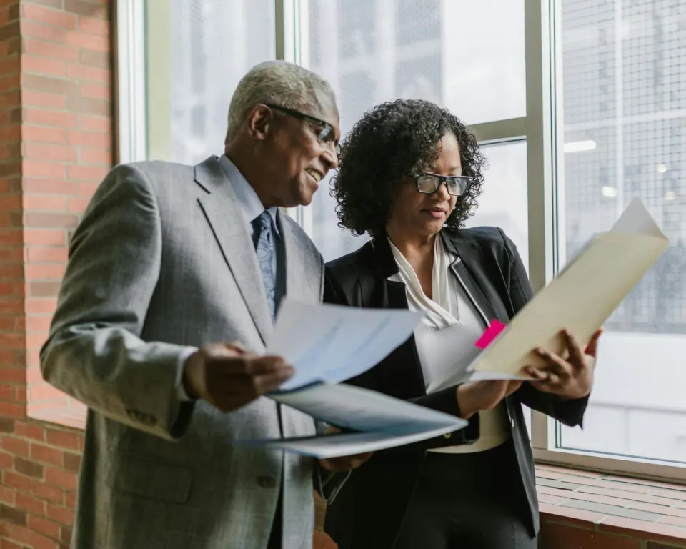 Two senior leaders read through a document together by a window.