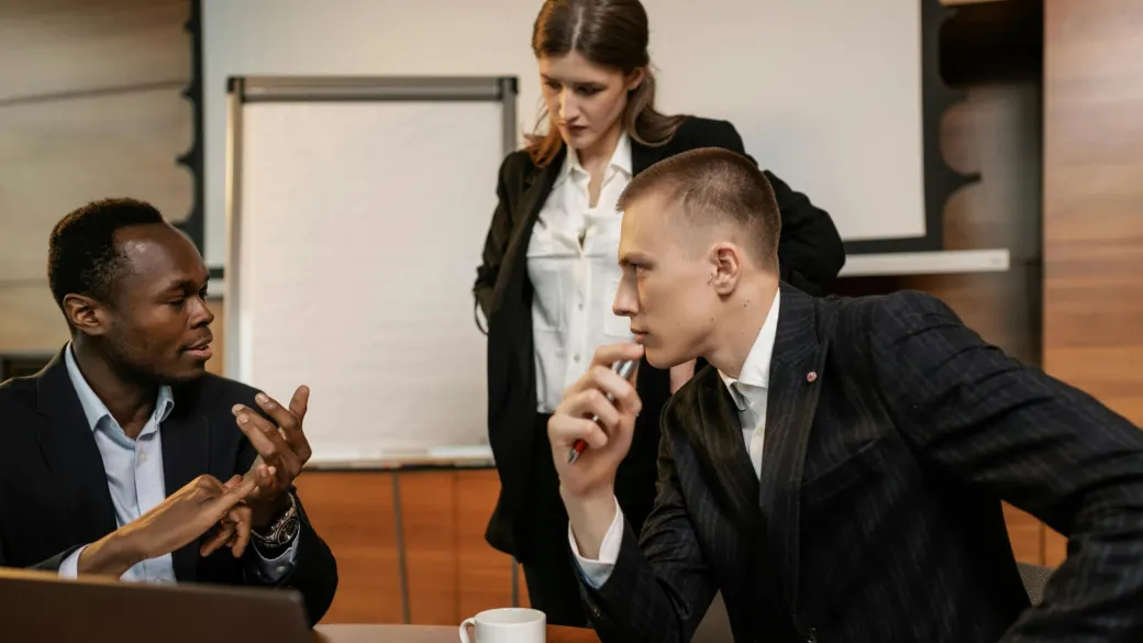 Three colleagues in a pointed discussion across a meeting table.